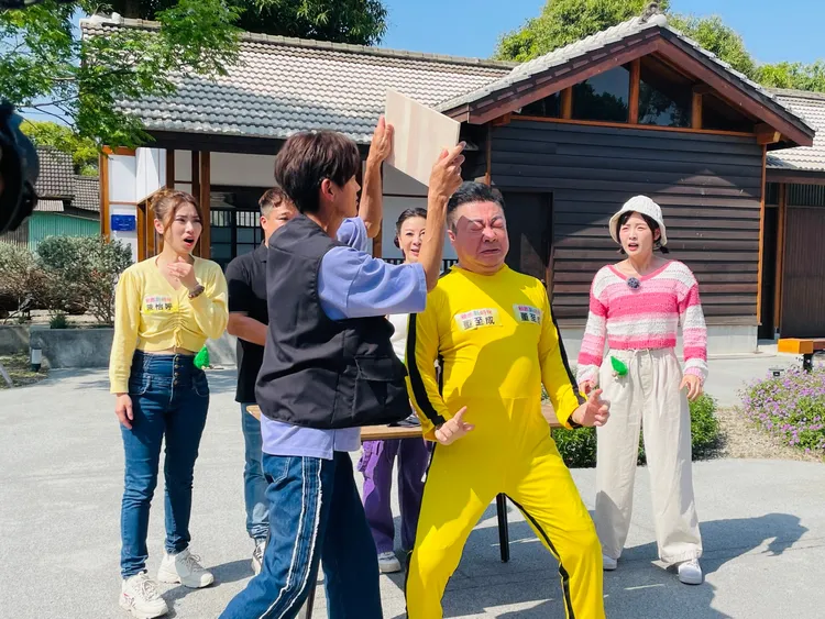 董至成（右）穿著超大號黃色功夫服，扮成「中年李小龍」進場，用手與腳快速有力要劈斷阿翔手上拿的木板。民視提供
