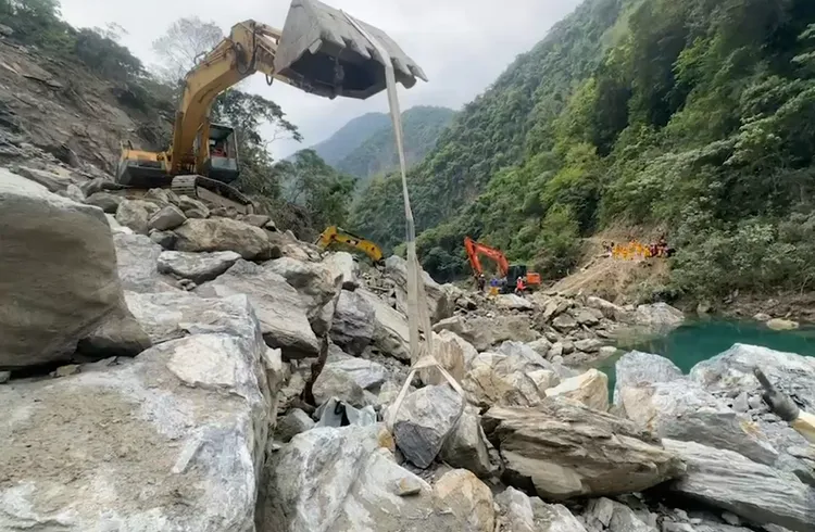 砂卡礑現場用大型挖土機將遺體從石塊堆中拉出。消防署提供