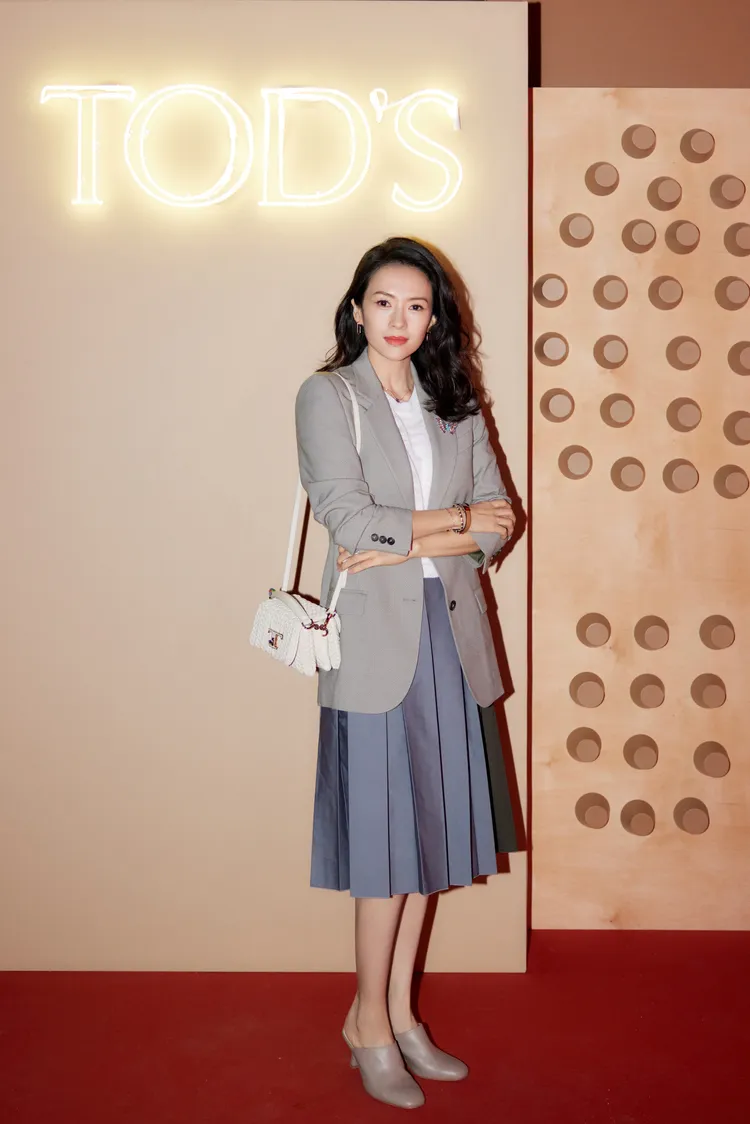 章子怡穿著西裝外套、百摺半身裙搭配白色編織紋路的T Timeless手袋。品牌提供