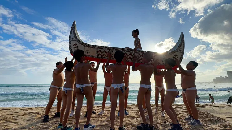 椰油國小小朋友在美國夏威夷海邊，高舉蘭嶼拼板舟留下美麗鏡頭。照片取自顏子矞老師臉書