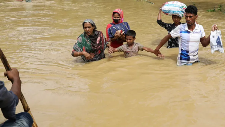在洪水中，一家5口帶著糧食手牽手走向救生艇。路透社