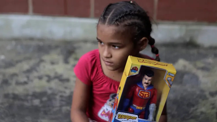 在2022年12月27時，一名女童手持馬杜洛總統的「超級鬍子」公仔，這是卡拉亞卡（Carayaca）社區分發的聖誕禮物。翻攝自《紐約郵報》

