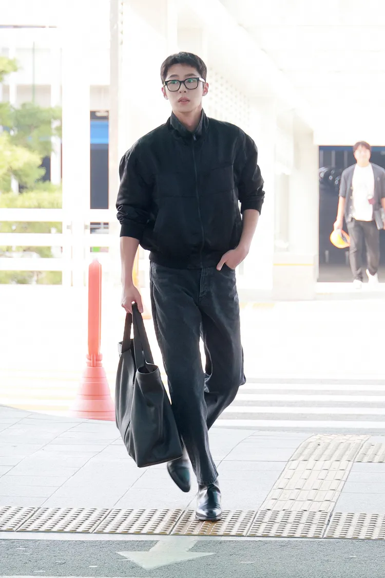 李宰旭的機場時尚是以SAINT LAURENT緞面Teddy外套與仿舊黑色寬鬆剪裁牛仔褲，搭配Wyatt滑面皮革切爾西靴及Y系列托特包，搭上黑框眼鏡，有種略帶知性的帥氣魅力。
