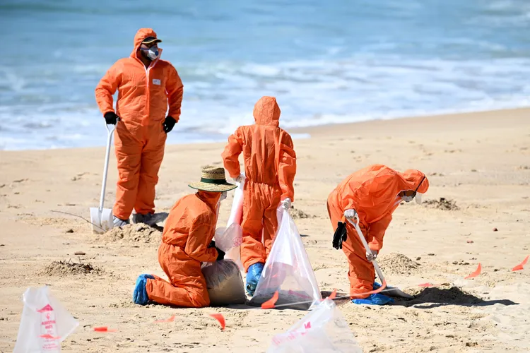 工作人員緊急清除海灘上的黑球。路透