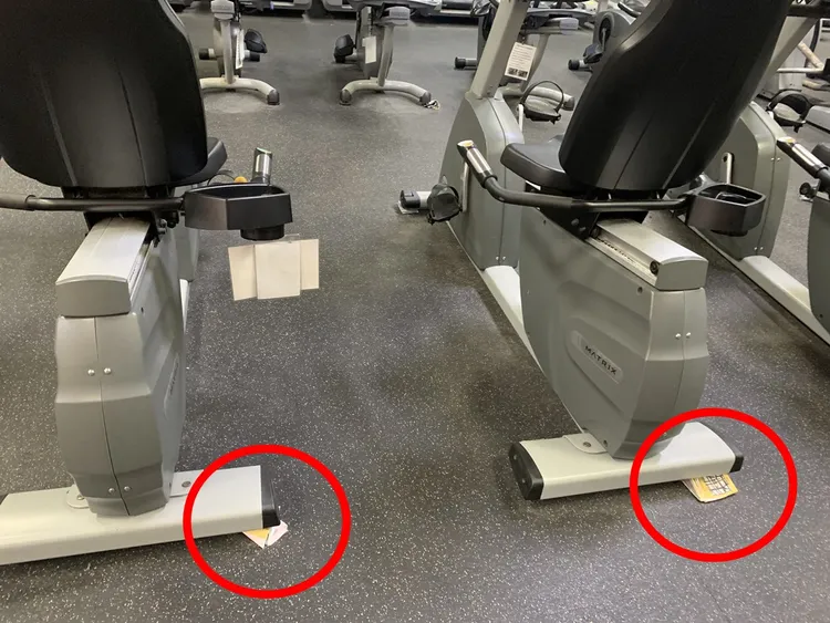 運動中心多台健身器材不穩，用厚紙片將底部墊高。陳怡君提供