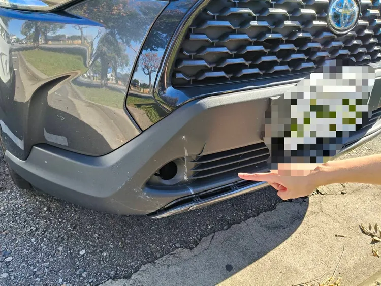 轎車前保險桿被掉落的怪手窗框砸破。民眾提供