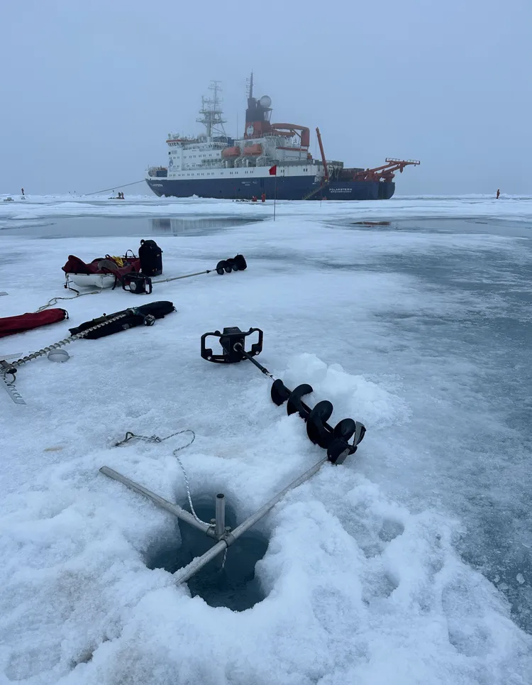使用鑽洞機、鋸子進行鑿洞後，將科儀設備固定在海冰上進行海流量測，背景為極星號。國海院提供