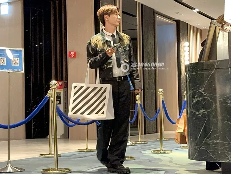 SJ隊長利特提著off white帆布袋，和女助理搭電梯到飯店大廳櫃台訂房。特勤中心攝