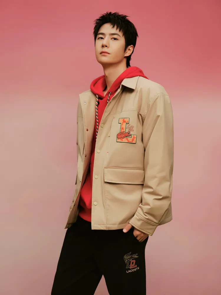 王一博穿著LACOSTE卡其色外套、紅色帽T搭配黑色運動褲。品牌提供