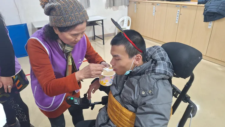 八里愛心教養院志工為院生準備暖呼呼的湯圓，志工秋菊阿姨(左)一口一口餵著院生。社會局提供