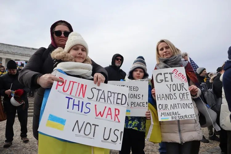 俄羅斯全面入侵烏克蘭將屆3年，烏克蘭旅美社群22日在華府發動紀念遊行。圖為參與民眾，手持「伊隆（馬斯克）少碰我們國家的礦產」（右）及「發動這場戰爭的是普丁，不是我們」（左）的手寫海報。中央社