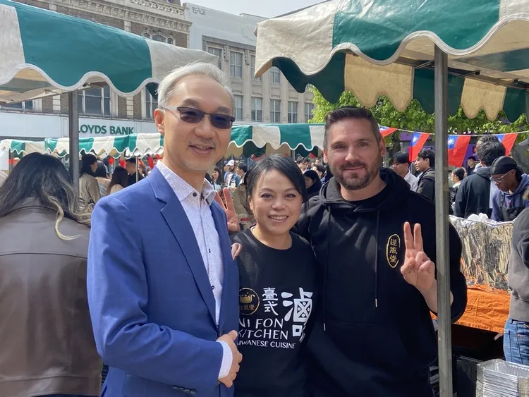 旅居英國的台灣人劉佳昕（中）和來自羅馬尼亞的男朋友一起賣台式滷味。駐英國代表姚金祥（左）參觀她的攤位後，一起合影。 中央社