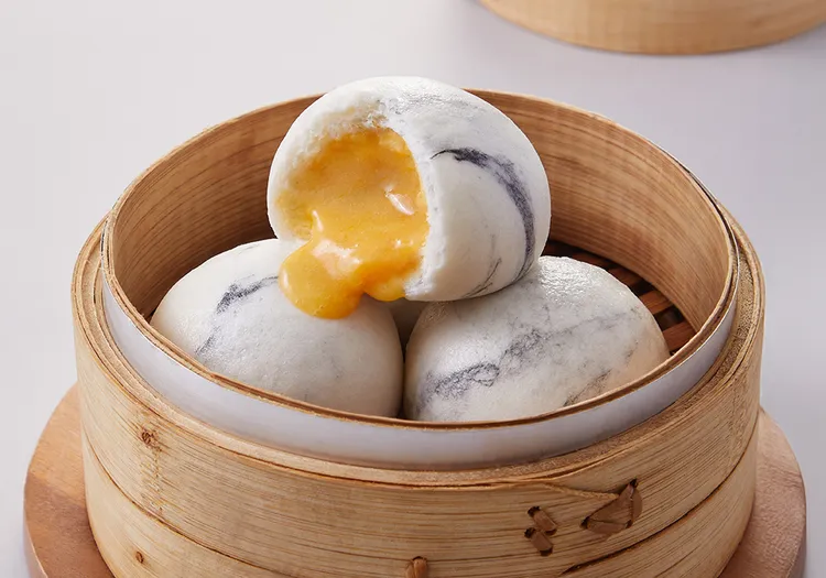 「黃金流沙包」融合創意與經典點心。可可紋理麵皮包裹鹹蛋黃、奶油、椰漿內餡，一咬即爆漿流出，建議搭配茶品享用，口感豐富、餘韻綿延。業者提供