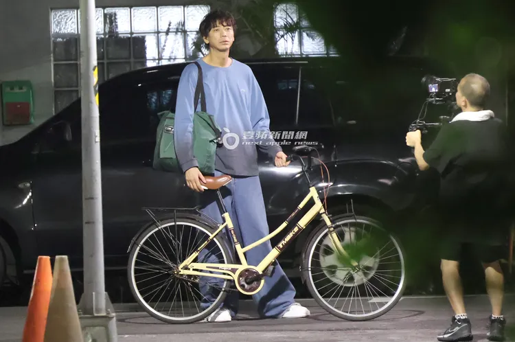 信背著一袋衣服在巷弄裡牽淑女車。特勤中心攝