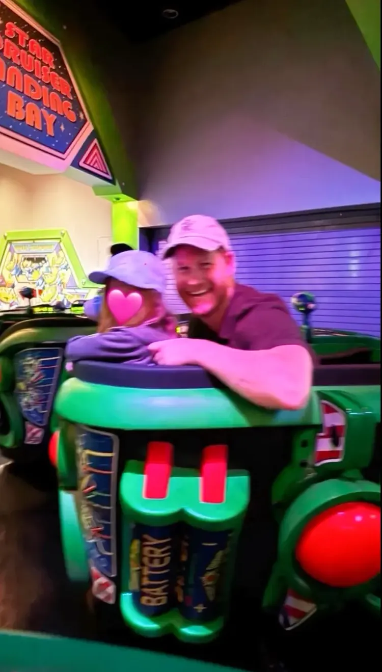 哈利陪女兒玩遊樂設施，露出開心的笑容。