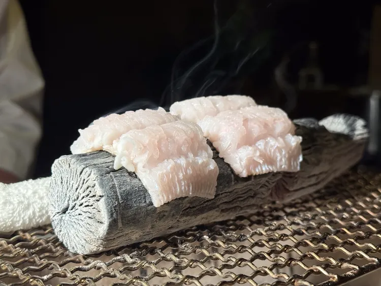 長岡主廚重視五感體驗，板前用菊炭淺炙魚皮，聲響與香氣勾人食欲。豊漁餐飲集團提供