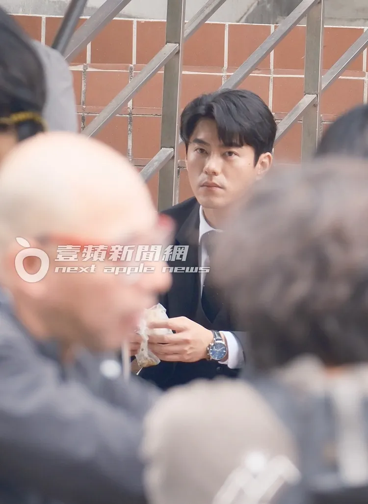 李程彬坐在永樂市場的戶外階梯上，若有所思等待拍戲。特勤中心攝