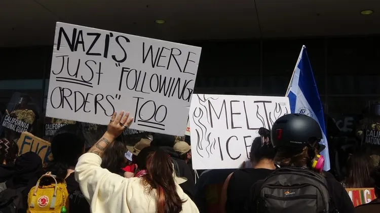 洛杉磯數百人群眾聚集在聯邦政府大樓前，抗議移民暨海關執法局（ICE）突襲掃蕩非法移民，反對總統川普派國民兵進駐。一名示威者拿著標語抗議國民兵「納粹當年也說只是奉命行事」。 中央社