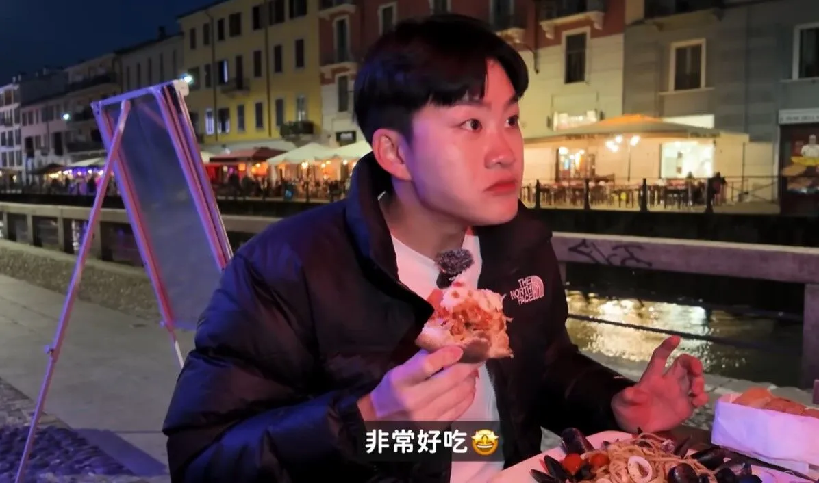 Joeman在義大利米蘭運河旁用餐,吃到美味披薩,他下意識看向左手邊座位說「非常好吃」,被疑帶女友同遊。翻攝Joeman YT