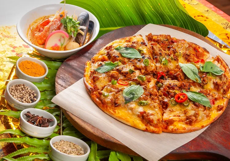 現煮「南洋叻沙麵」（左）湯頭辛香，入口微帶椰香甜味；「打拋豬肉披薩」（右）將經典熱炒搬上餅皮，是令人驚喜的東西合璧創意之作。台北凱撒大飯店提供