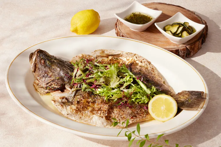 「炭烤現流鱸魚佐義大利檸檬香草醬」嚴選現流鱸魚以直火炭烤，外酥內裡多汁柔嫩，搭配南義經典檸檬香草醬提鮮，佐以醋漬櫛瓜增添層次與酸香。台北喜來登大飯店提供