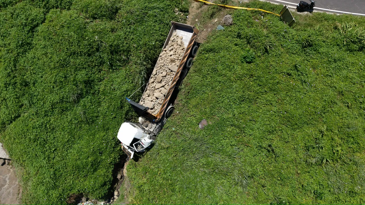 砂石车失控冲出道路,直至卡进边坡草丛后才停下。翻摄照片