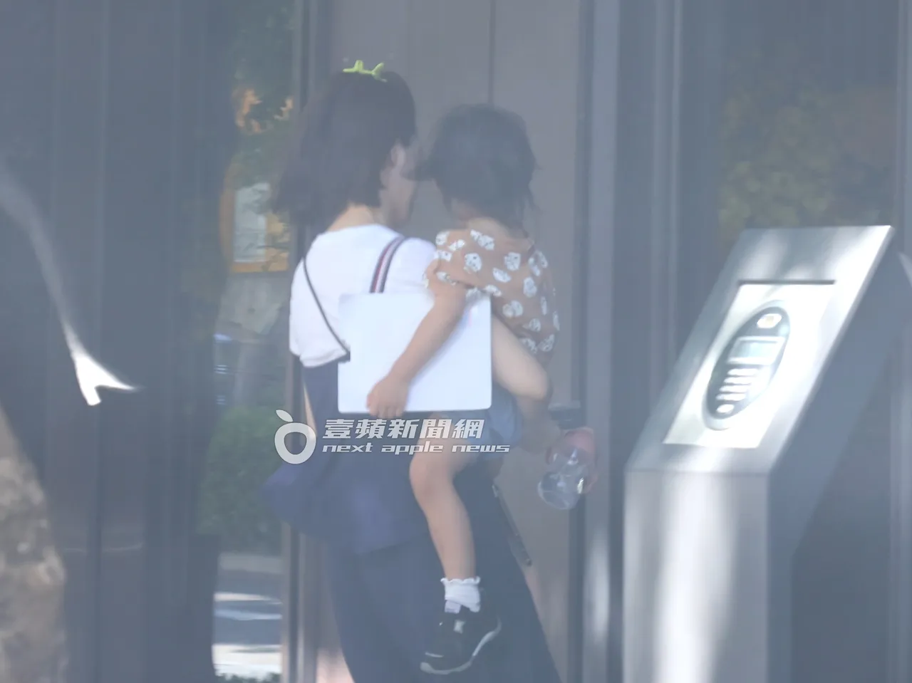 女子一手拿手機和黃玉米的水壺及一本書,一手抱著拿卡片的黃玉米走進豪宅。特勤中心攝