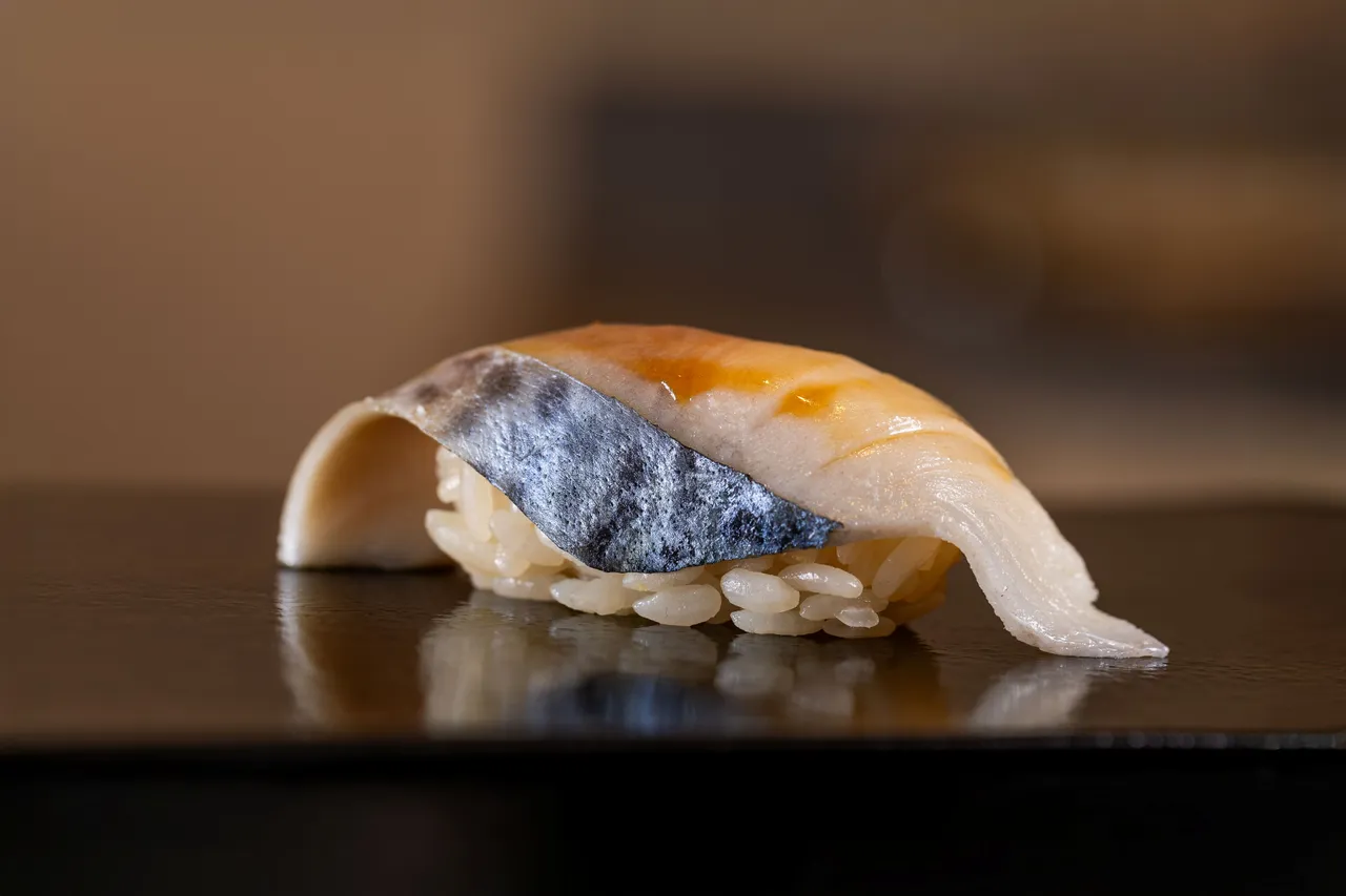醋漬鯖魚握壽司,取自魚身腹部,依據魚貨狀況與油脂分布調整醃漬比例,因亮皮魚腥味較重,刻意搭配常溫醋飯,平衡入口體驗,讓鯖魚的軟嫩與鮮味在舌尖綻放層次。業者提供