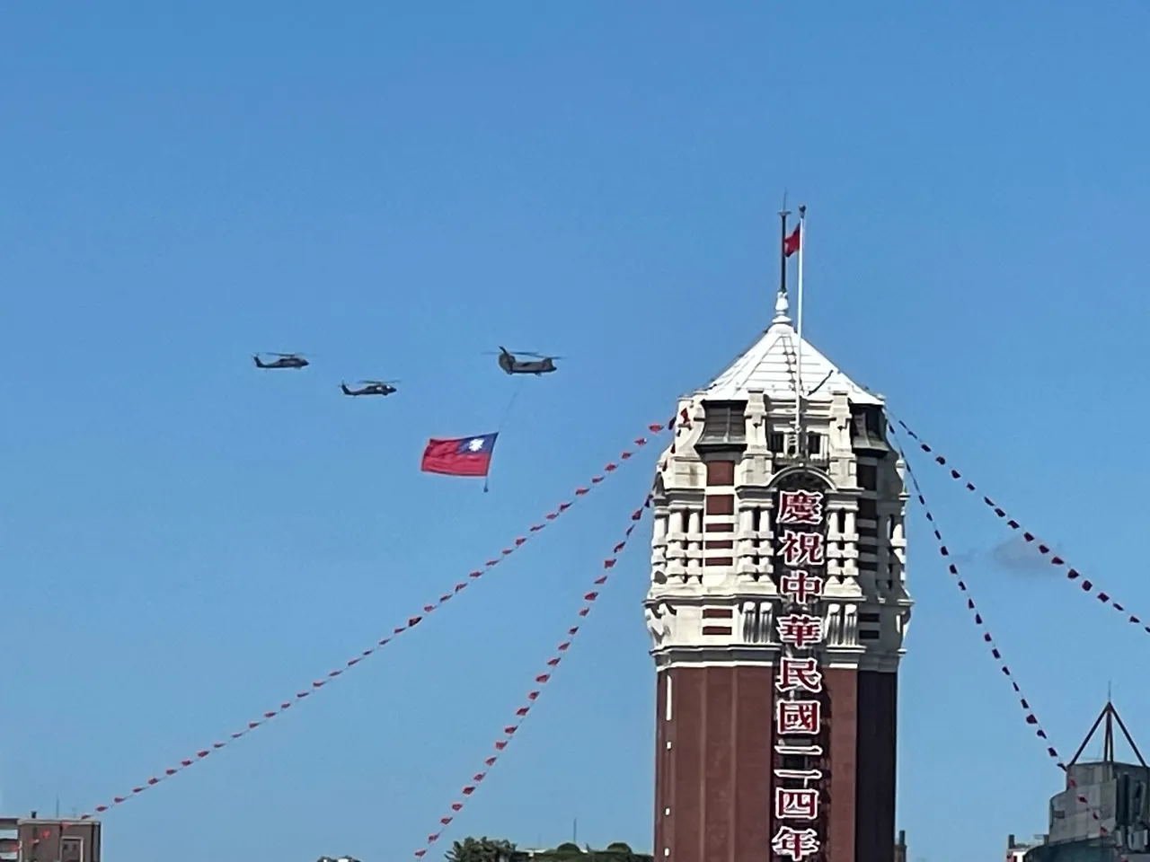 114年國旗大會今天隆重登場,陸軍一架CH-47SD契努克重型直升機吊掛巨幅國旗,伴隨2架UH-60M黑鷹直升機飛越總統府前方廣場上空,有民眾拍下國旗總統府同框的精彩畫面。讀者提供