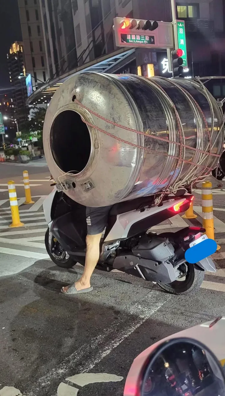 機車載著一個銀色水塔桶，大型水塔擋住騎士身影。翻攝自臉書爆料公社