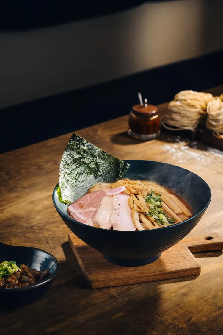 台南西門店限定登場的「醬油煮干清湯拉麵」，以慢火熬煮的雞湯為底，融入日式醬油的深邃香氣，加入產自台南的虱目魚鬆，湯色清亮、味道醇厚。業者提供