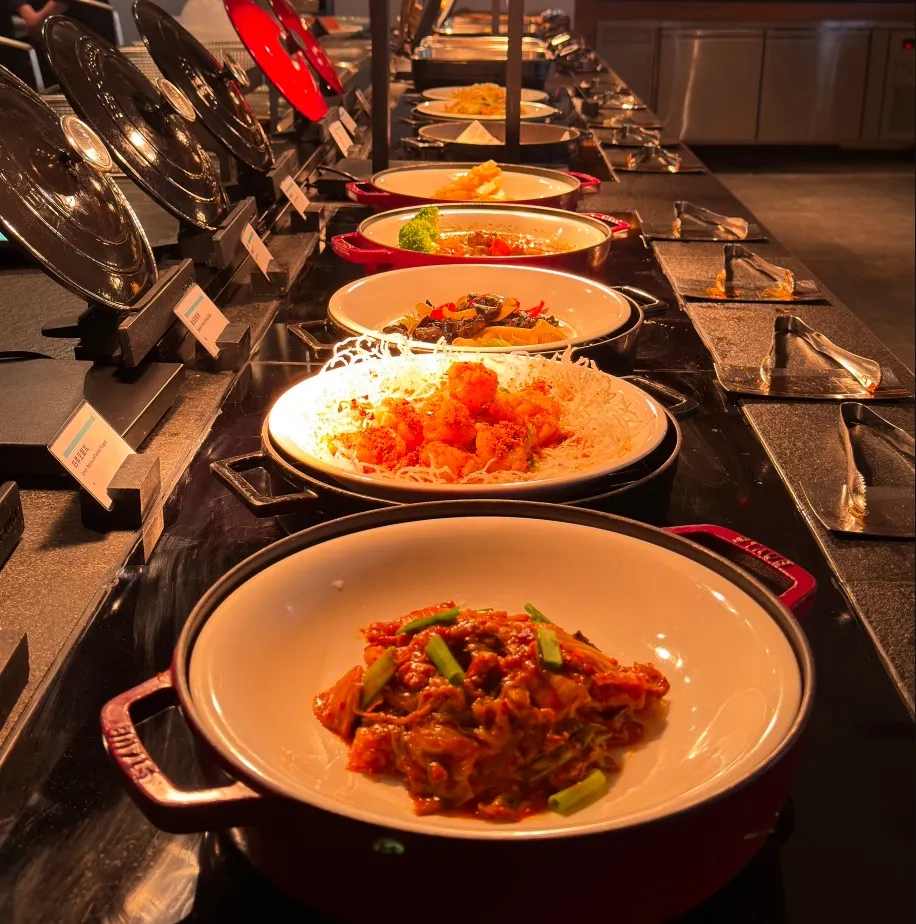 熱食可選擇韓式泡菜燒肉、爐烤蘿勒醃漬雞腿排、鄉村燉肉，到清炒時蔬、素燉什錦野菇，兼顧葷素與營養平衡。另有清粥熱湯區，提供地瓜清粥、皮蛋肉絲粥、味噌湯與多樣醬菜，展現台式與西式融合的早餐文化。業者提供