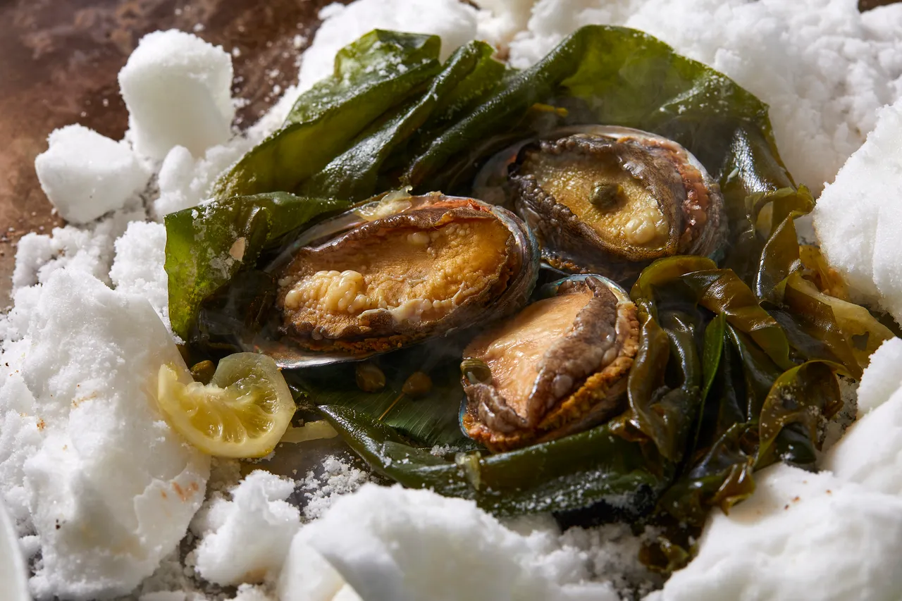 「鹽蒸鮑魚」是  Ukai  鐵板燒料理中傳承逾 40 年的經典招牌菜。以細緻的鹽層包覆鮑魚，以低溫緩慢蒸煮，完整保留海味鮮甜。The Ukai Taipei提供