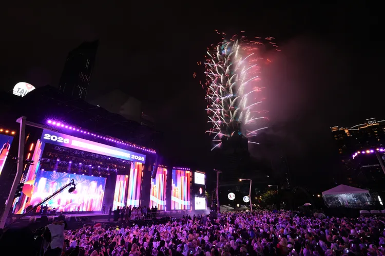 隨著煙火持續沿塔身綻放，台北101在低煙設計下仍保有清晰輪廓，現場觀眾在舞台燈光與夜空火光交錯中迎接新年。彭欣偉攝