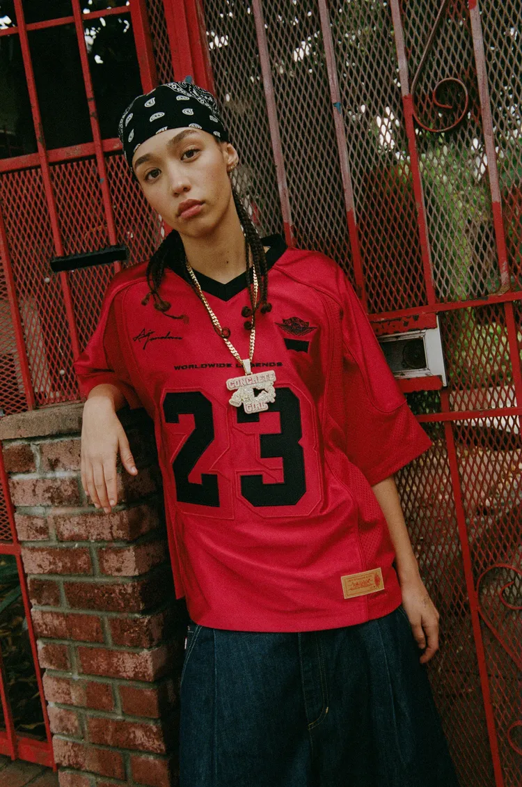 足球球衣採用紅色霧面與亮面拼接設計，細節處加入聯名運動員標籤。品牌提供