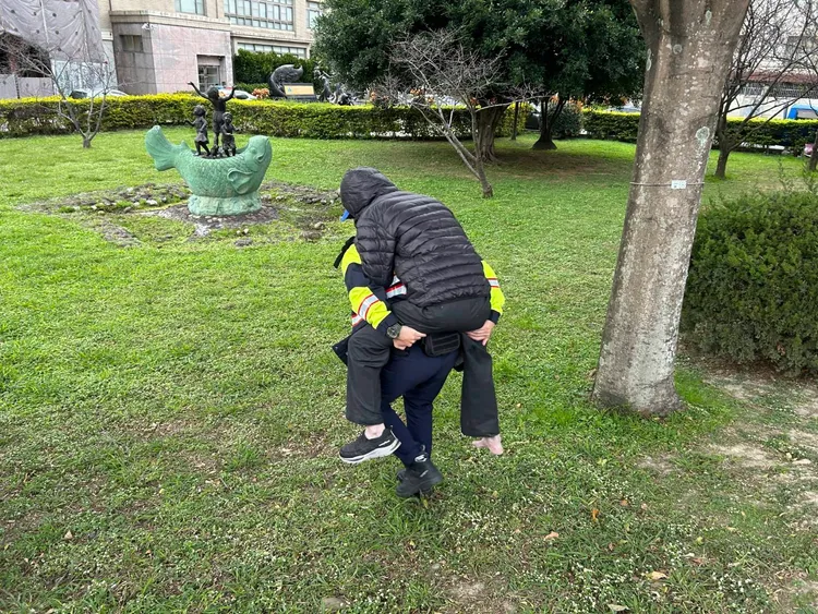 警員揹著老翁穿越河堤草坪。中壢警分局提供