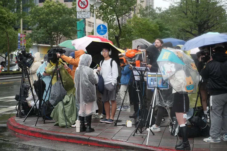 觀眾撐著雨傘、穿雨衣，站在第一排朝聖。彭欣偉攝