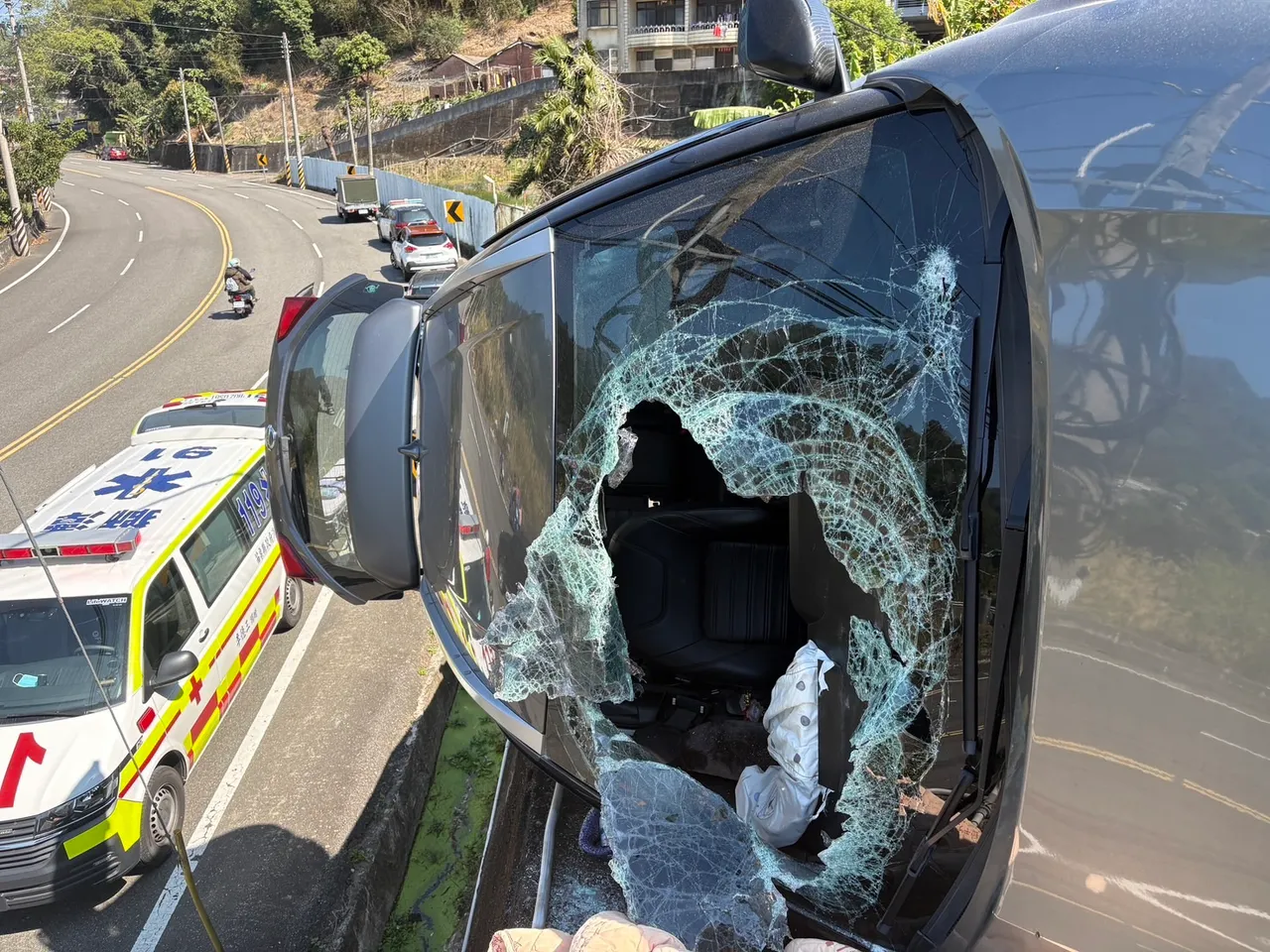 高男轎車前擋風玻璃破了一個大洞，側翻懸在邊坡上。民眾提供