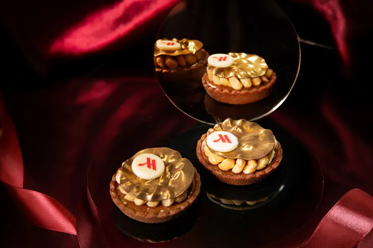 台北萬豪「魔幻巧刻」雙人下午茶，充滿黑金華麗質感的「榛果阿澤莉亞巧克力塔」，酥脆的巧克力派皮中，填入了以35%阿澤莉亞牛奶巧克力、無糖榛果醬與大溪地香草精心調製的榛果甘納許，塔面鋪滿了金黃的烘烤榛果。業者提供