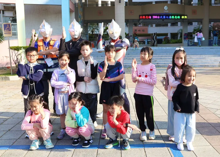 新上國小校長王彥嵓(後中)、家長會長蘇守懌（後左）與家長化身「超人力霸王」，站在校門前熱情迎接返校的孩子。翻攝畫面