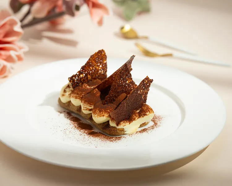 「經典義大利提拉米蘇」層次分明的乳酪灑上可可粉，斜插著如蟬翼般輕薄透明的巧克力蕾絲片，用當代時尚擺盤展現經典義式幸福滋味。每道360元。台北遠東香格里拉提供