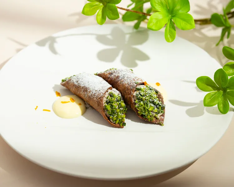 「馬沙拉酒奶油甜餡煎餅捲 瑞可達起司 糖漬柑橘 開心果」」焦脆餅殼裡充滿絲滑起司內餡，兩端沾滿開心果碎，甜潤爽脆，充滿地中海風情。每道380元。台北遠東香格里拉提供