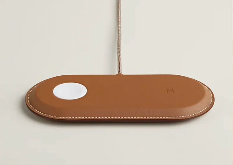 Hermès推出Paddock系列MagSafe充電器，以Swift小牛皮包覆並搭配品牌經典馬鞍縫線設計，中央白色磁吸區對應iPhone充電位置，將原本實用的科技配件升級為精品級桌面單品。Hermès官網
