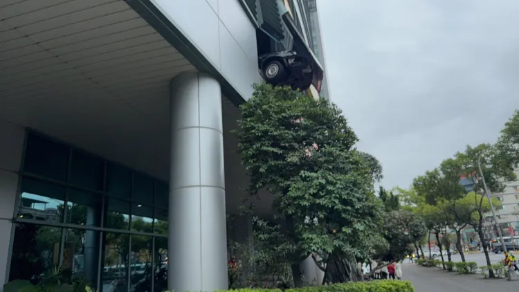 板橋縣民大道上台電大樓2樓停車場外牆突出一輛汽車半身，引來用路人議論，原來是駕駛誤踩油門導致意外。翻攝畫面