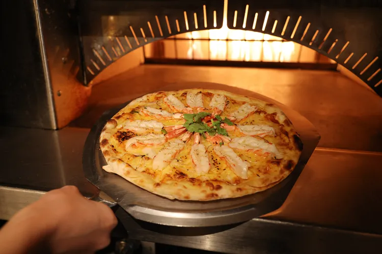 充滿南洋風情的「酸辣蝦披薩」是以酸辣醬鋪底，搭配鮮蝦、香茅與辣椒等辛香料，再撒上濃郁起司高溫窯烤而成，並由服務人員定時派送，熱騰騰上桌。台北晶華提供