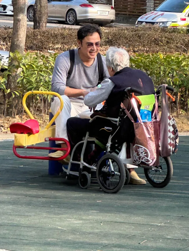 明道身穿灰色上衣、戴著墨鏡，神情專注地陪伴母親，不時彎身交談、逗她開心，眼神流露滿滿關愛。sherryching822授權提供