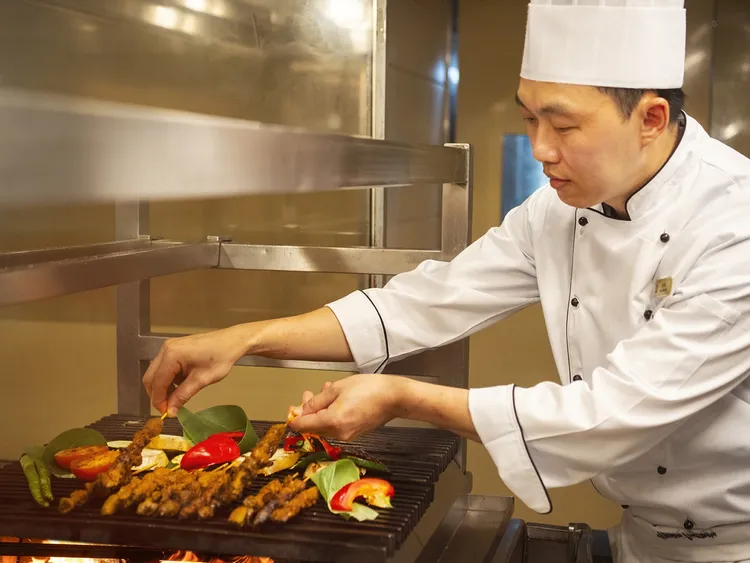 黃志偉主廚現場示範「羊肉沙嗲」烤製技藝，憑藉職人控火功力，迅速鎖住肉質鮮甜，復刻南洋街頭最正統的碳烤層次。台北遠東香格里拉提供