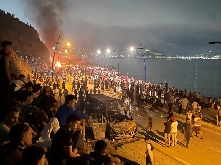 大批移民聚集在一輛遭焚毀的汽車周圍，等待機會越境進入西班牙飛地休達。路透