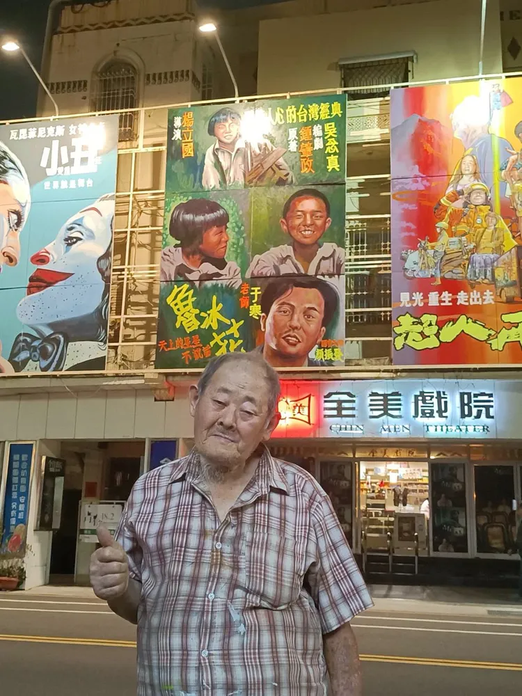 台灣國寶級手繪電影看板畫師顏振發與《魯冰花》大型手繪看板合影。翻攝自今日全美戲院粉專