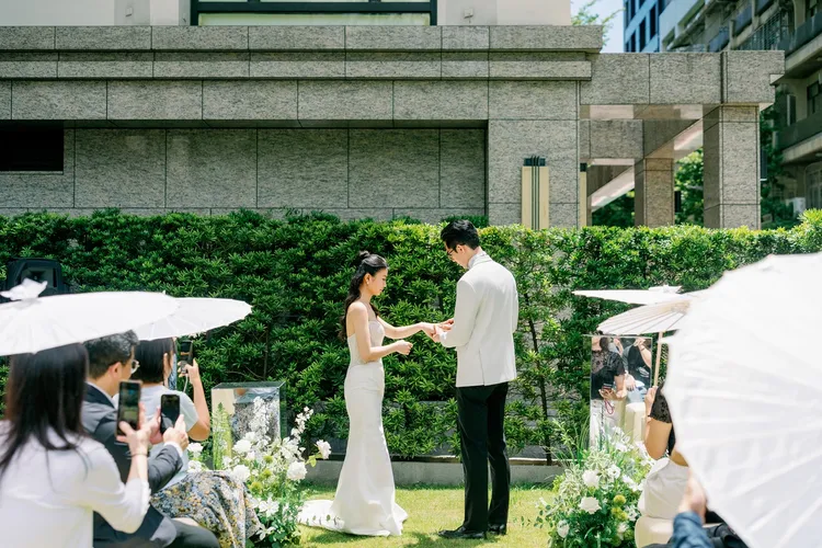 純白紙傘、翠綠樹籬與鏡面花藝相伴，在親友溫柔的注視下戴上誓言婚戒，儀式感滿溢。業者提供